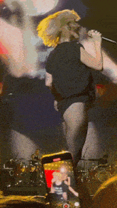 a woman singing into a microphone while a phone takes a picture