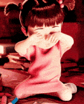 a little girl in a pink dress covering her eyes with her hands