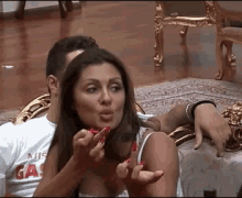 a man and woman are sitting on a couch and the woman is wearing a shirt that says gas