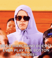 a man wearing a hoodie and sunglasses is sitting in a crowd .