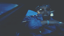 a man wearing sunglasses and a bandana is sitting in a car with the name the maw on the bottom