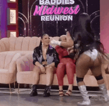 two women are sitting on a couch with the words baddies midwest reunion behind them
