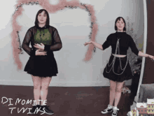 two women are dancing in front of a wall that says dynamite twins on it