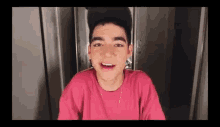a young man wearing a pink shirt and a black hat is talking to the camera .