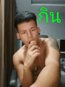a shirtless man with a tattoo on his arm eating a sandwich