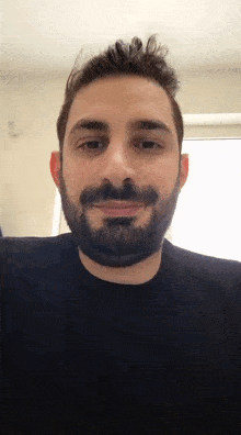 a man with a beard is wearing a black shirt and smiling