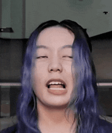 a woman with blue hair is making a funny face with her eyes closed and her mouth open .