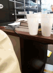 two styrofoam cups sit on a desk with a km sticker on it