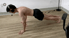 a shirtless man is doing push ups on a wooden floor while wearing headphones .