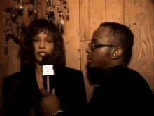 a woman is talking into a microphone while a man watches .