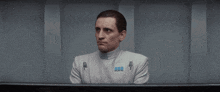 a man in a white uniform with a blue badge on his chest is sitting in a dark room .