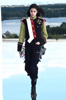 a model walks down the runway at a fashion show wearing a jacket with a cross on it