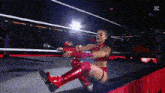 a woman in red boots is kneeling in a wrestling ring holding a sword .