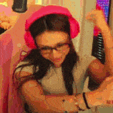 a woman wearing pink headphones and glasses flexing her muscles