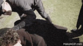 a man is laying on top of another man in a field while a group of people are standing around .