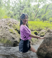 a girl in a purple shirt is standing in a stream
