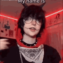a person with horns and glasses is wearing a red hoodie and a bandana around their neck .