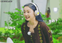a woman wearing headphones and a brown sweater is smiling and looking at the camera .
