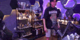 a man wearing a paranoke shirt is standing in front of a microphone in a room filled with figurines .