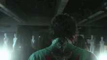 a woman in a green dress is standing in a dark room with mannequins