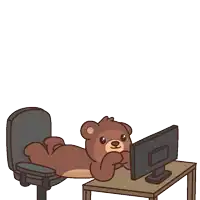 a teddy bear is laying on a desk looking at a computer monitor