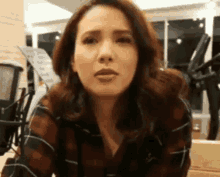 a woman in a plaid shirt is making a funny face and looking at the camera .