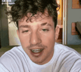 a man with curly hair is wearing a white shirt and smiling