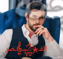 a man with a beard and a ring on his finger is sitting in a blue chair