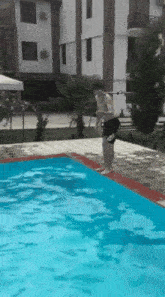 a man jumps into a swimming pool with a building in the background