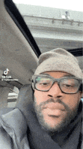 a man with glasses and a beanie is sitting in a car .