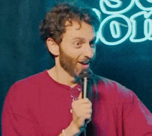 a man in a red shirt is holding a microphone in front of a sign that says comedy .