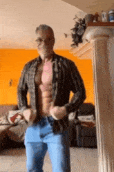 a man without a shirt is standing in a living room with his shirt off .