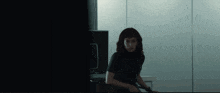 a woman in a black shirt is sitting in a dark room looking at something