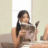 a woman is sitting at a table holding a magazine .