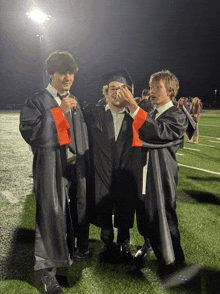 three graduates are posing for a picture on a field at night