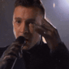 a man in a suit is singing into a microphone while holding his hand to his face .