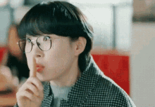 a woman wearing glasses and a plaid jacket is holding her finger to her mouth .