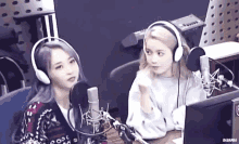 two women wearing headphones are sitting in front of microphones in a radio studio .