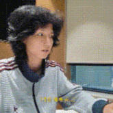 a woman wearing a grey jacket with red stripes on the sleeves is sitting at a table