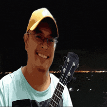 a man wearing a hat and glasses holds a guitar