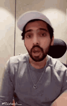 a man with a beard is wearing a hat and a necklace with the name raidaah on the bottom