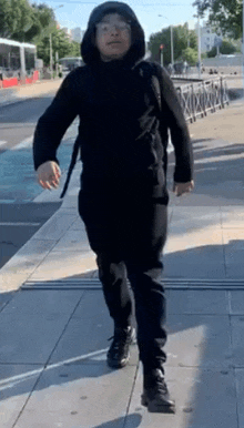 a man in a black hoodie and sunglasses is walking down a sidewalk .