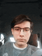 a young man wearing glasses is sitting in a car with a shirt that says ' abercrombie & fitch ' on it