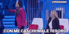 a man in a pink jacket is standing next to a woman in a black suit and says con me caschi male tesoro .