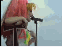 a woman singing into a microphone with pink hair