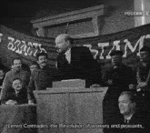 a man stands at a podium in front of a banner that says lenin comrades