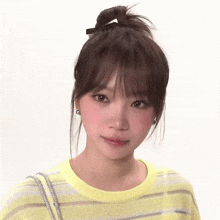 a woman wearing a yellow striped sweater has her hair in a bun .