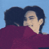 a man in a red shirt is hugging another man with a blue sky in the background