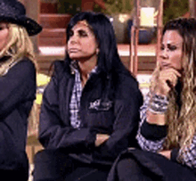 three women are sitting next to each other on a chair . one of the women is wearing a cowboy hat .