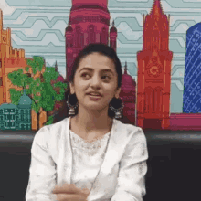 a woman is sitting in front of a painting of buildings